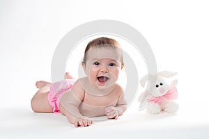 Little girl smiling with a toy rabbit lies on white background.