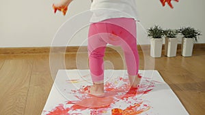 Little girl with smudgy paint fingers draws on a large sheet of white paper sitting on the floor