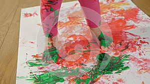 Little girl with smudgy paint fingers draws on a large sheet of white paper sitting on the floor