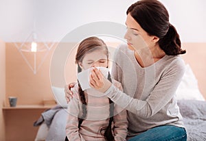 Little girl sneezing while sitting with her mother