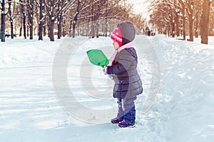 Little girl with a snow shovel playing outside in winter