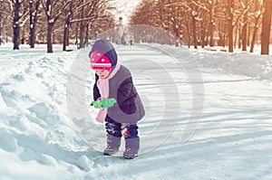 Little girl with a snow shovel playing outside in winter