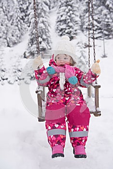 Little girl at snowy winter day swing in park