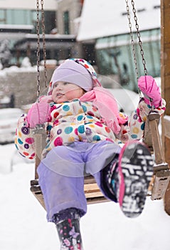 Little girl at snowy winter day swing in park