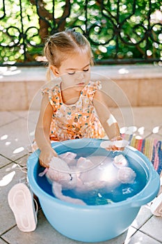 Little girl soaping up a soft toy in a bowl on the balcony