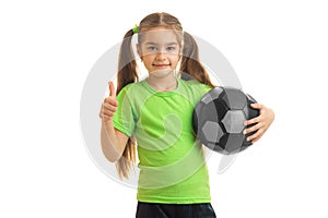 Little girl with soccer ball in hands looking at the camera showing thumbs up
