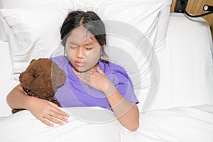 Little girl with sore throat holding toy bear abd lying on bed