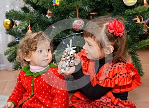 The little girl in the Spanish suit shows to the one-year-old little sister a toy about a New Year tree