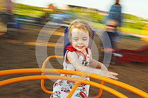 Little girl spinning on a children`s carousel among the playground.