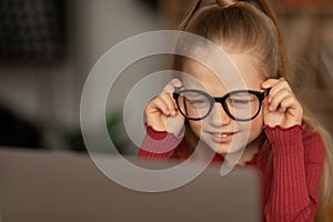 Little Girl Squinting Eyes Using Laptop Wearing Glasses At Home