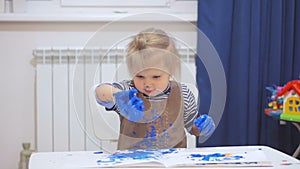 A little girl stained her hands and clothes in paint while drawing. The child carefully examines the dirty hands.