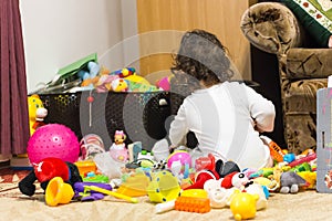 Little girl standing with back in a pile of toys
