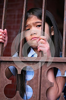 Little girl standing behind iron bars