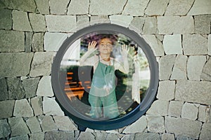 Little girl standing behing round window, pressing nose against the glass.