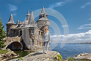 Little girl standing on a big rock near the lake against old vintage castle