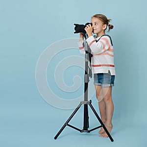 Little girl standing on her toes looking in the camera on tripod, taking picture