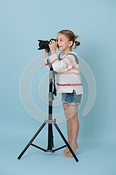 Little girl standing on her toes looking in the camera on tripod, taking picture