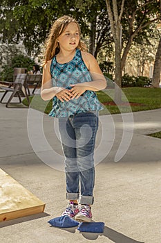 A little girl standing holds her hands together while looking away with a curious expression