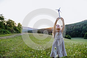 Little girl standing in nature with model of wind turbine. Concept of ecology future and renewable resources.