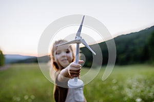 Little girl standing in nature with model of wind turbine. Concept of ecology future and renewable resources.