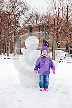 Little girl standing near the snowman.