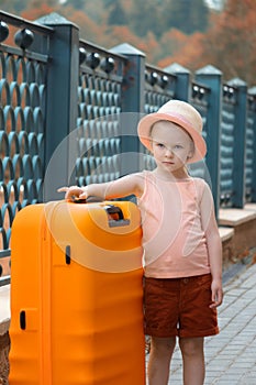 A little girl is standing next to a large orange suitcase. A beautiful portrait of a child.