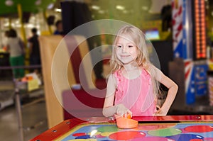 Little girl standing and playing air hockey at indoor amusement park