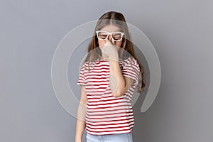 Little girl standing ribbing her eyes, takes off glasses, felling eyes hurt and headache.