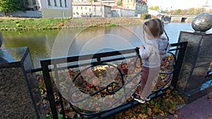 Little girl standing on riverside near city river in autumn