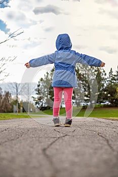 Little girl standing on a road in the park in spring. Child from behind