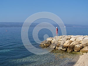 Little girl standing on the rocks watching the sea