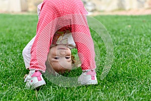 Little girl standing smiling with her head upside down on the grass