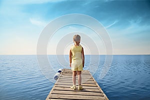 Little girl standing at wooden pier and looking to the sea.