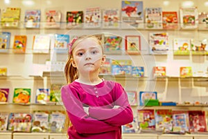 Little girl stands with arms folded on chest in book department