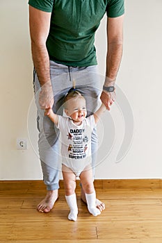 Little girl stands and holds daddy's hands in the room