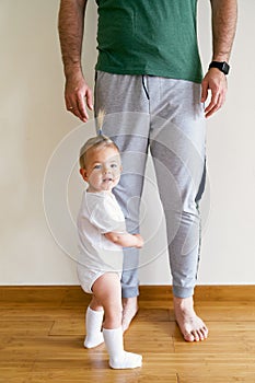 Little girl stands and holds on to daddy& x27;s leg in the room