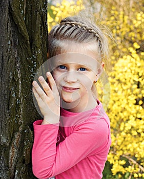 Little girl stands leaning against a tree