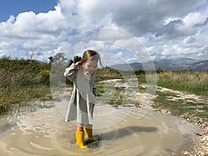 Little girl stands in a muddy puddle straightening her hair with her hand