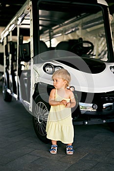 Little girl stands near a six-seater golf cart in the parking lot