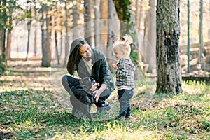 Little girl stands next to her mother squatting and stroking a dog