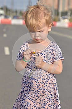 A little girl stands on the road with a flower in her hands