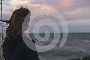 Little girl stands on the shore and looks at the sea