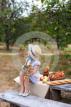 Little girl in straw hat with bouquet of flowers sits on bench on picnic in garden. Summer vacation. Copy space. Nature, healthy f
