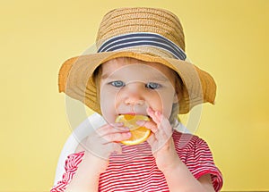 Little girl in a straw hat eats a lemon on a yellow background