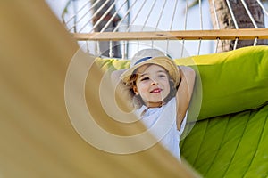 Little girl in straw hat lying in hammock and enjoying summer exotic vacation.