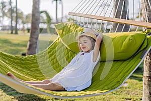 Little girl in straw hat lying in hammock and enjoying summer exotic vacation.