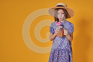 Little girl in a straw hat and sunglasses is smiling on a yellow background. child girl in a blue dress is holding a