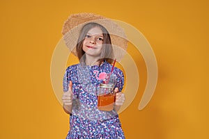 Little girl in a straw hat and sunglasses is smiling on a yellow background. child girl in a blue dress is holding a