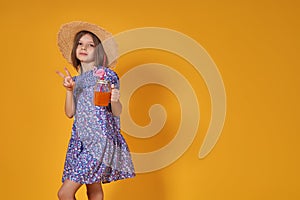 Little girl in a straw hat and sunglasses is smiling on a yellow background. child girl in a blue dress is holding a