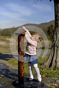 The little girl stretches her hands to the fountain.